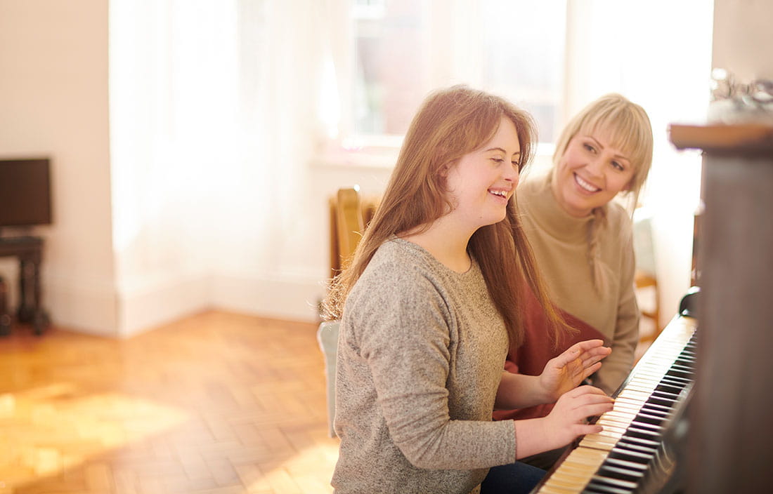 Child playing the piano while their mother watches and smiles.